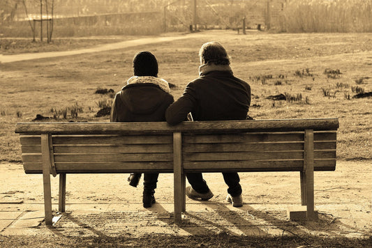 A sepia toned photograph of a couple sitting on a park bench.  They are facing away from the camera and wearing winter jackets.