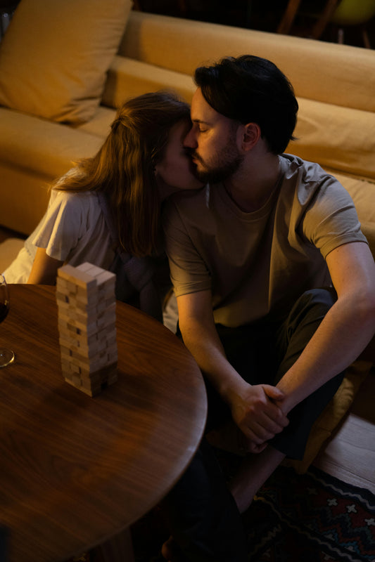 a man and woman snuggle on the floor in front of a round wooden table that holds a game of Jenga they completed during their at home date night.