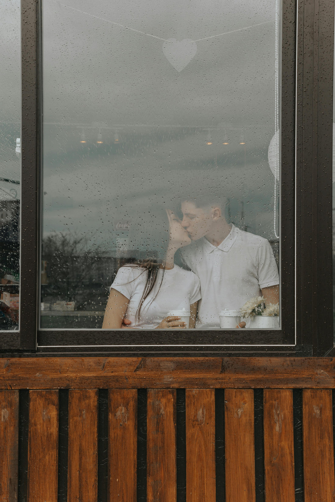 couple kissing in a coffee shop window on a rainy day.